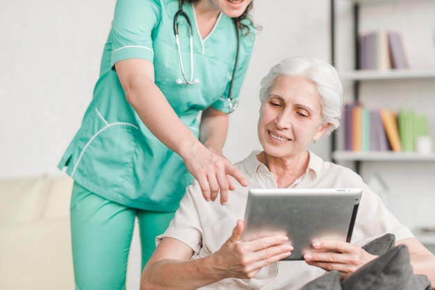 Krankenschwester, die dem älteren weiblichen Patienten auf digitaler Tablette etwas zeigt