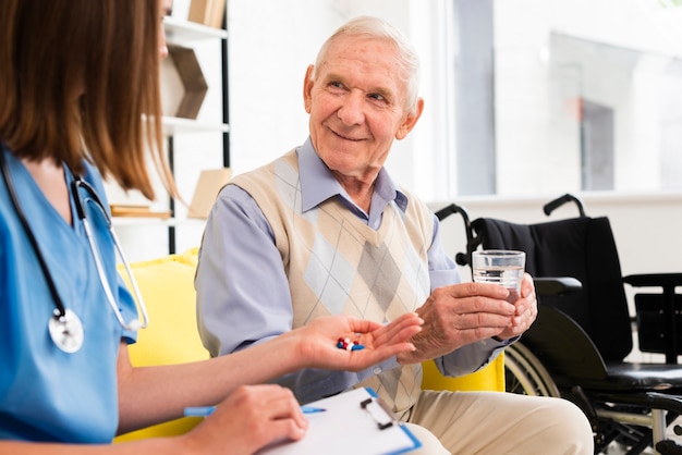 Krankenschwester, die dem alten Mann des smiley Pillen gibt