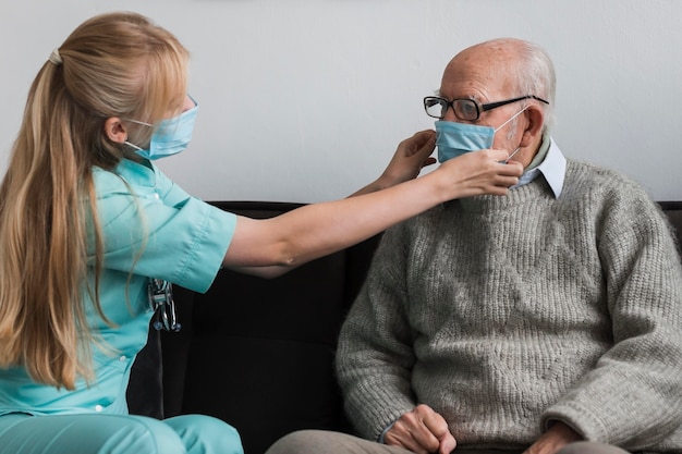 Krankenschwester, die die medizinische Maske des alten Mannes anpasst