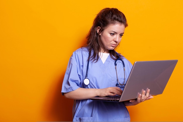 Krankenschwester, die Technologie auf einem modernen Laptop verwendet und Uniform trägt