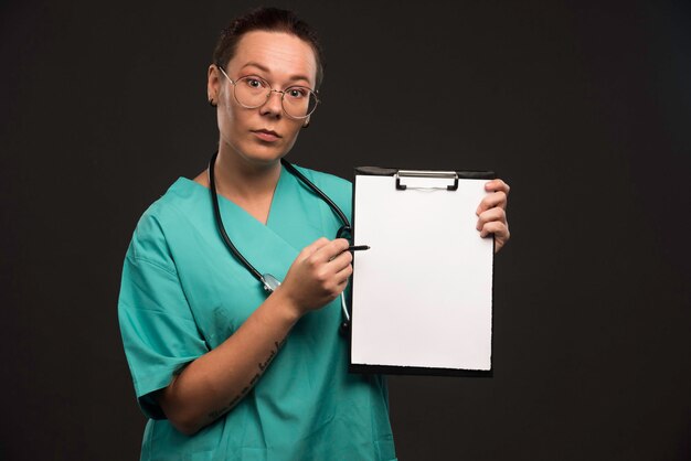 Krankenschwester in grüner Uniform zeigt die Geschichte des Patienten und macht Präsentation.