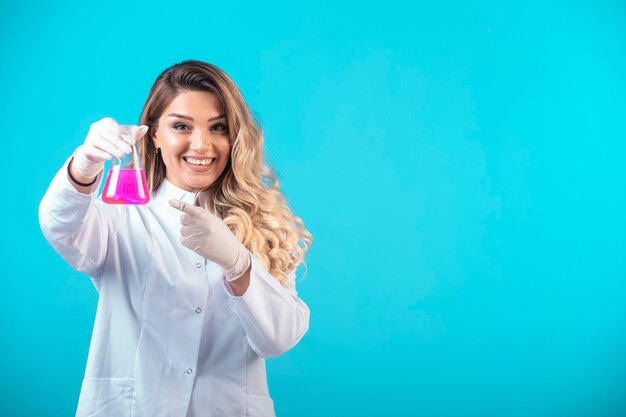 Krankenschwester in weißer Uniform hält einen Chemiekolben mit rosa Flüssigkeit und fühlt sich positiv