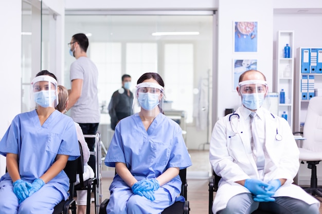 Krankenschwestern und Arzt mit weißem Kittel und Gesichtsmaske als Sicherheitsvorkehrung gegen den Ausbruch des Coronavirus im Wartebereich des Krankenhauses