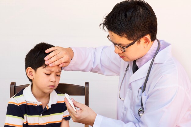 Kranker asiatischer Junge, der vom männlichen Doktor über weißem Hintergrund überprüft wird