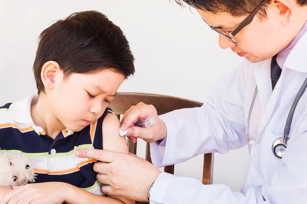 Kranker asiatischer Junge, der von männlichem Doktor über weißem Hintergrund behandelt wird