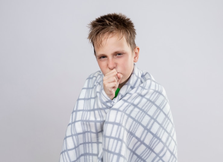 Kostenlose Foto kranker kleiner junge in decke gewickelt, der sich unwohl fühlt, über weißer wand stehend zu husten