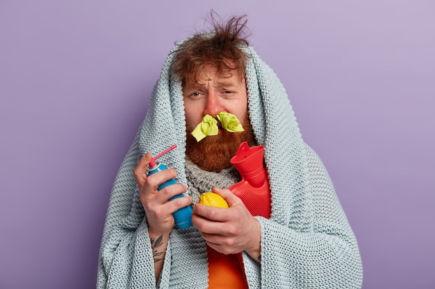 Kostenloses Foto kranker mann in warmer kleidung mit spray für nase, zitrone und wassersack