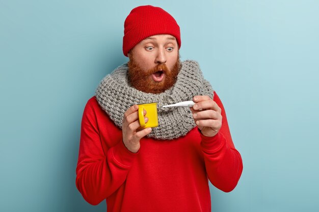 Kranker Mann in warmer Kleidung mit Thermometer und Tasse