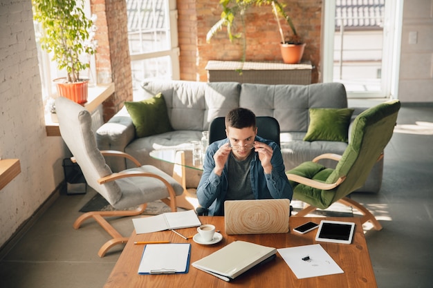 Kostenloses Foto kreativer arbeitsplatz - organisierter arbeitsplatz nach belieben zur inspiration. mann, der im büro in bequemer kleidung, entspannter position und unordentlichem tisch arbeitet. wählen sie die gewünschte atmosphäre - ideal klar oder chaos.