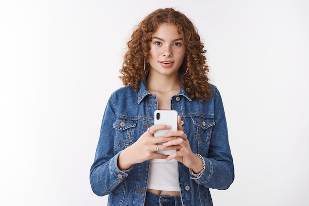 Kreativer attraktiver freiberuflicher Fotograf smm Mädchen Rotschopf hält Smartphone-Look fasziniert fotografieren Sie mit der Telefonkamera, stehender weißer Hintergrund fokussiert