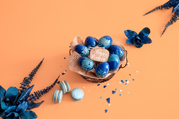 Kreatives Osterlayout aus bunten Eiern und Blumen auf Blau.