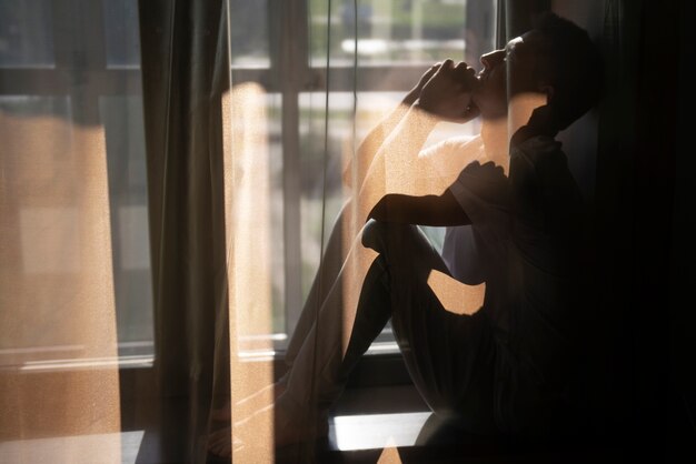 Kreatives Porträt des Mannes mit Vorhängen und Schatten vom Fenster