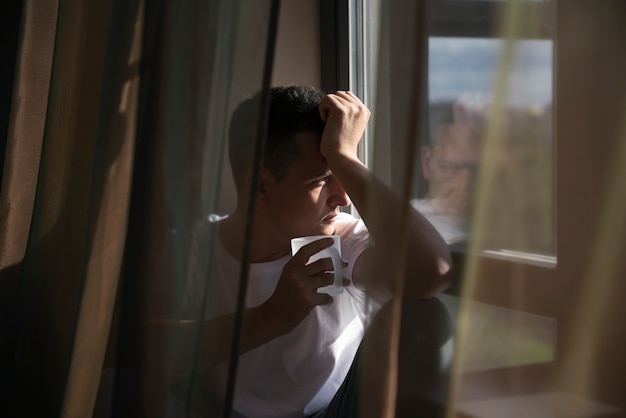 Kreatives Porträt des Mannes mit Vorhängen und Schatten vom Fenster