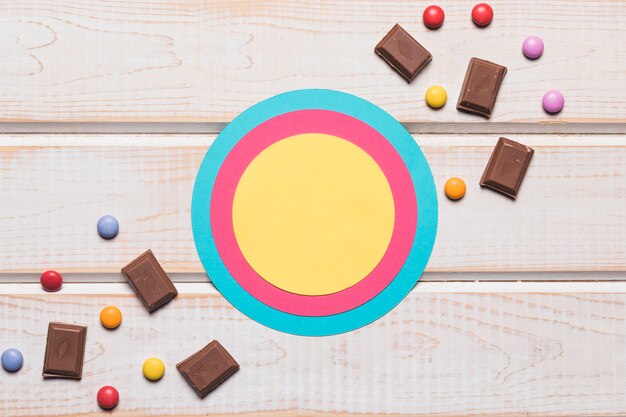 Kreisrahmen mit Schokoladenstücken und Edelsteinsüßigkeiten auf hölzernem Hintergrund