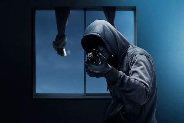 Krimineller Mann in versteckter Maske, der die Schrotflinte zeigt, während er das Haus in der Nacht ausraubt