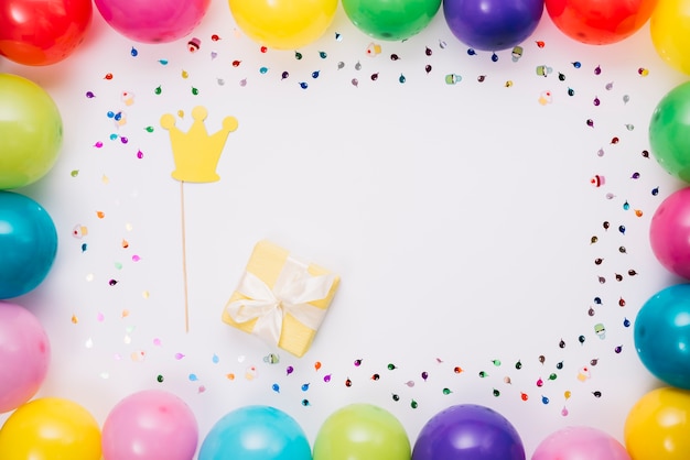 Kostenloses Foto kronenstütze und geschenkbox im bunten rahmen mit konfetti und luftballons