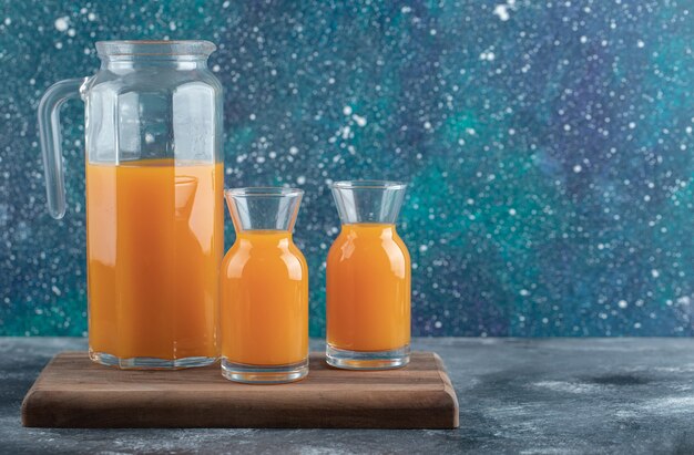 Krug und Gläser Orangensaft auf Holzbrett.