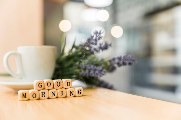 Kubikblöcke des gutenmorgens mit Tasse Kaffee auf hölzernem Schreibtisch