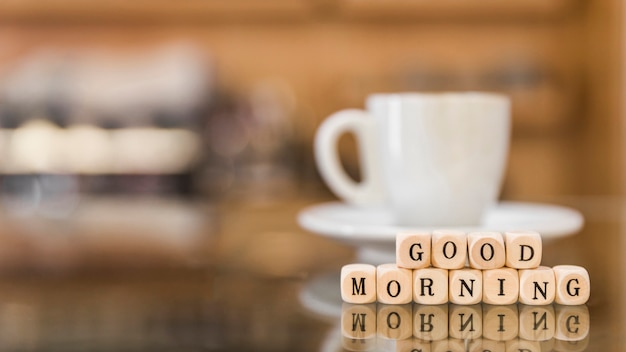Kubikblöcke des gutenmorgens mit tasse kaffeereflexion auf glas
