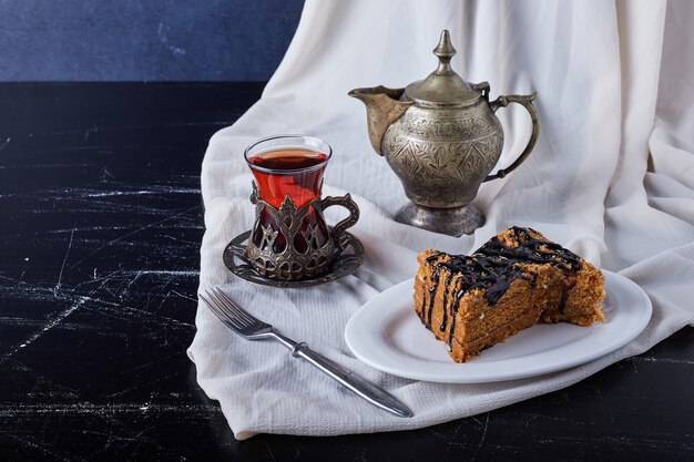 Kuchenscheibe in einem weißen Teller mit Schokoladensirup und Tee.