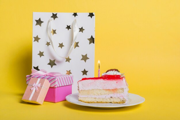 Kuchenscheibe mit beleuchteter Kerze; Einkaufstasche in Sternform; und Geschenkbox auf gelbem Hintergrund