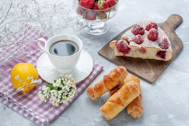 Kuchenscheibe mit frischen roten Erdbeeren, süßen Armreifen und einer Tasse Kaffee auf hellem Schreibtisch, süßes Backkeks-Keksgebäck