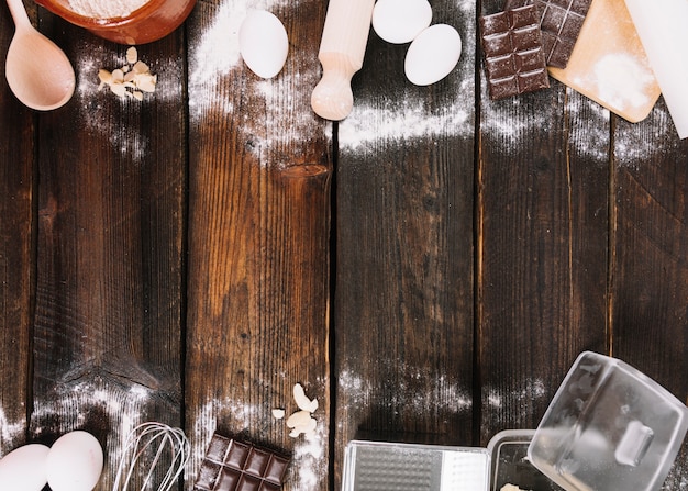 Küchengerät und Bestandteile für backenden Kuchen auf hölzernem Plankenhintergrund