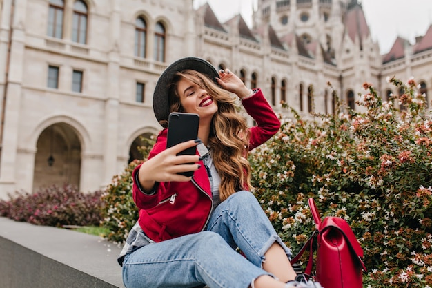 Kühlende Frau in Retro-Jeans, die Selfie mit geschlossenen Augen nahe Straßenblumen machen