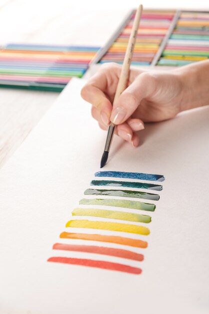 Künstler, der bunte Streifen mit Pinsel auf weißem Papier malt