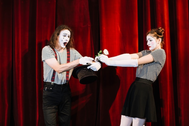 Künstler mit zwei Pantomimen, der am Stadium vor rotem Vorhang durchführt