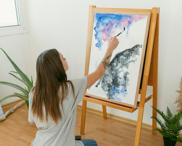 Künstlerfrau malt auf Leinwand von hinten Schuss