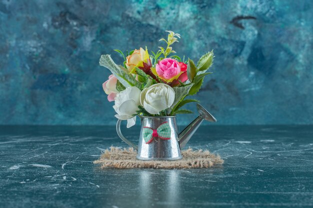 Künstliche Blumen in einer Gießkanne auf blauem Hintergrund.