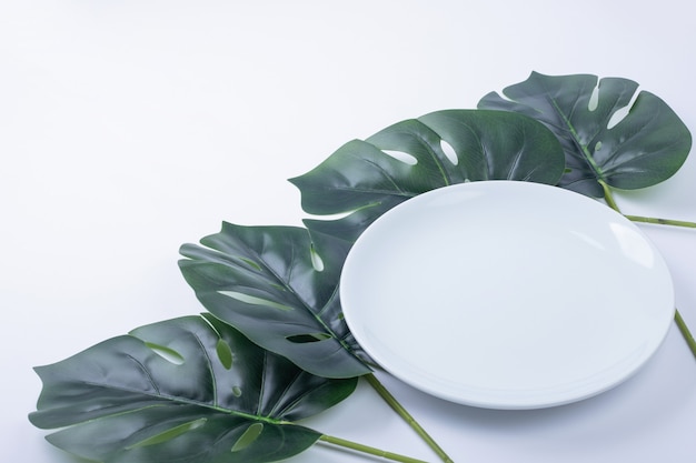 Künstliche grüne Blätter um weiße Platte.