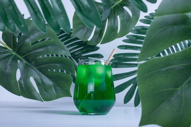 Künstliche grüne Blätter und Glas Saft auf weißem Tisch.