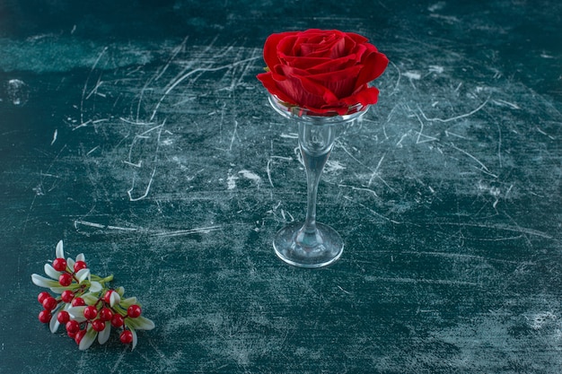 Künstliche rote rose in einem glassockel auf blauem hintergrund.