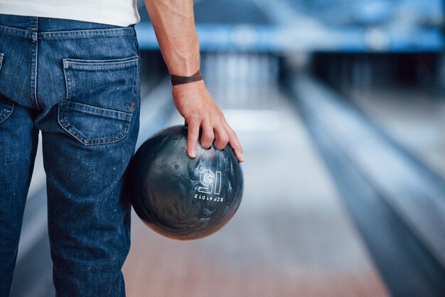 Künstliches Licht. Hintere Partikelansicht des Mannes in der Freizeitkleidung, die Bowling im Club spielt