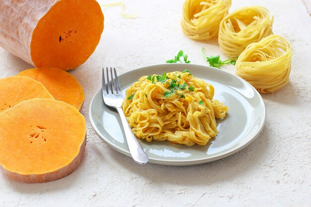 Kürbis Alfredo Fettucine Pasta in einer Keramikplatte mit frischen rohen Butternut-Kürbis-Scheiben. Herbstessen zum Mittagessen. Butternut-Kürbis-Rezept.