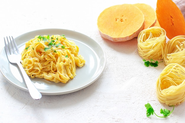 Kürbis Alfredo Fettucine Pasta in einer Keramikplatte mit frischen rohen Butternut-Kürbis-Scheiben. Herbstessen zum Mittagessen. Butternut-Kürbis-Rezept.