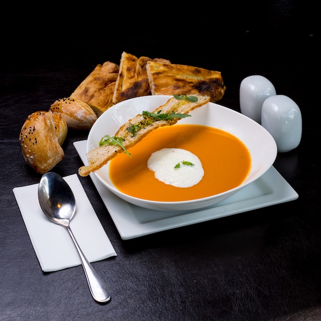 Kürbissuppe mit Milchschaum Brötchen Cracker Rucola Seitenansicht