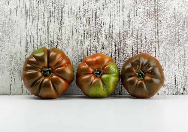 Kostenloses Foto kumato-tomaten auf weißer und schmuddeliger wand. seitenansicht.