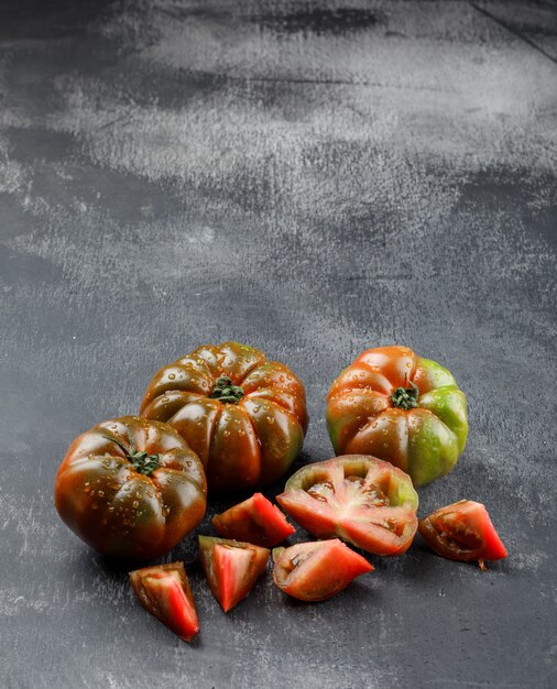 Kumato-Tomaten mit Scheiben auf grungy grauer Wand, hohe Winkelansicht.