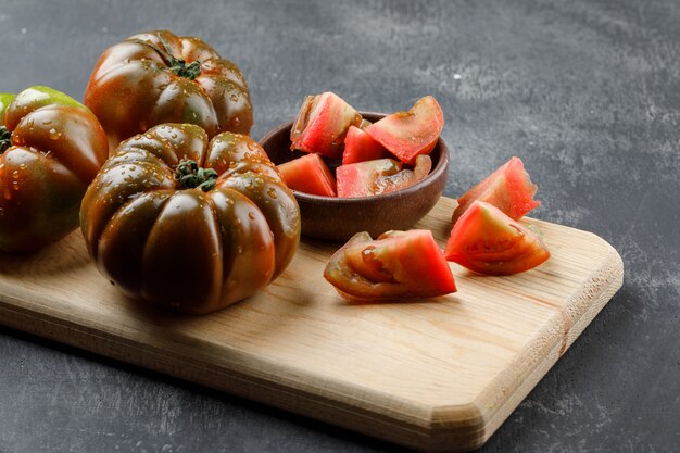 Kumato-Tomaten mit Scheiben in Platte auf Schmutz und Schneidebrettwand, hohe Winkelansicht.