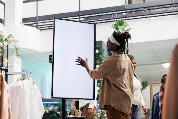 Kunde interagiert mit digitalem Smartboard im Bekleidungsgeschäft. Afroamerikanischer Mann tippt auf den leeren Bildschirm des Whiteboards, um Informationen über die neue Schuhkollektion im Einkaufszentrum zu lesen