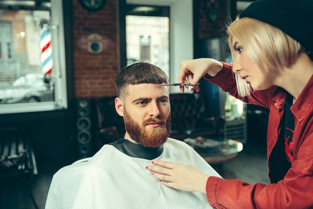 Kunde während der Bartrasur im Friseursalon. Friseurin im Salon. Geschlechtergleichheit. Frau im Männerberuf.