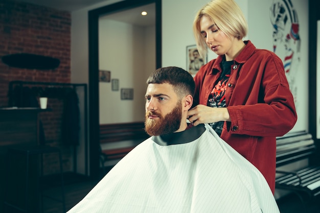 Kunde während der bartrasur im friseursalon. friseurin im salon. geschlechtergleichheit. frau im männerberuf.