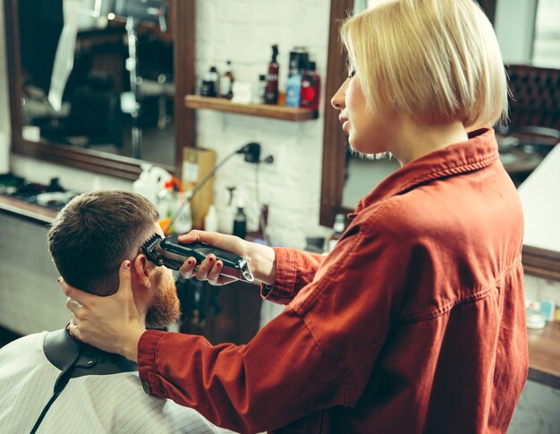 Kunde während der Bartrasur im Friseursalon. Friseurin im Salon. Geschlechtergleichheit. Frau im Männerberuf.