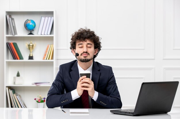 Kundendienst hübscher junger kerl im büroanzug mit laptop und headset schloss die augen mit kaffee