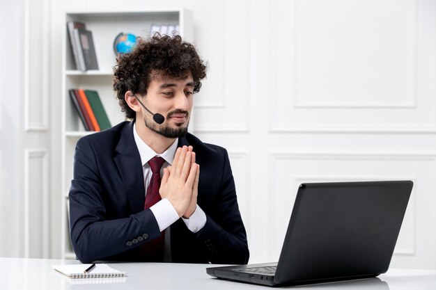 Kundendienst, hübscher junger Mann im Büroanzug mit Laptop-Headset, der mit den Händen zusammen betet