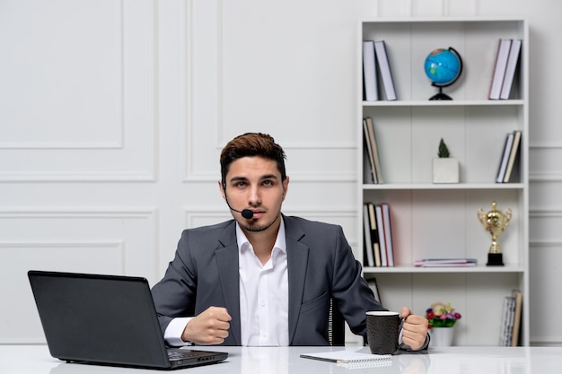 Kundendienst netter gutaussehender kerl im büroanzug mit computer mit dem headset und der tasse