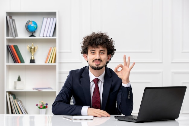 Kundenservice gelockter brünetter junger Mann im Büroanzug und roter Krawatte mit Laptop zuversichtlich